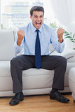 Victorious businessman cheering while sitting on sofa