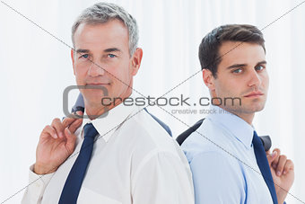 Serious businessmen posing back to back together while holding their jacket