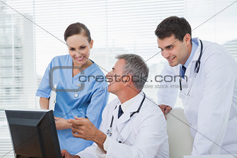 Cheerful doctors and surgeon working together on computer