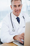 Smiling experienced doctor typing on his laptop