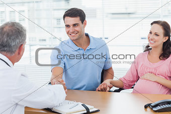 Smiling man shaking hands with his doctor while holding his expecting wifes hand