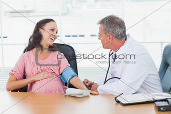 Doctor taking blood pressure of smiling pregnant patient