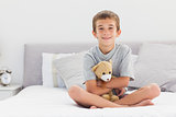 Smiling little boy sitting on bed holding his teddy bear