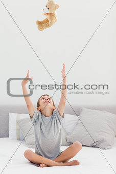 Little boy sitting on bed throwing his teddy bear to the ceiling