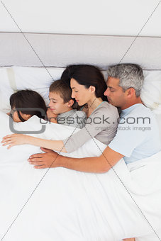 Parent sleeping with their children in bed
