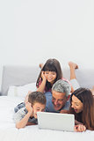 Happy family lying on bed using their laptop