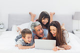 Cheerful family lying on bed using their laptop