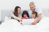 Smiling family lying in bed using their laptop