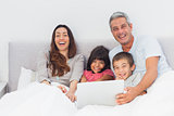 Happy family lying in bed using their laptop