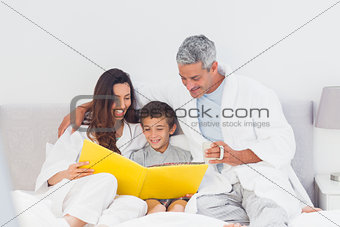 Parents with their son on bed looking together at photograph album