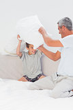 Father and son fighting together with pillows on bed