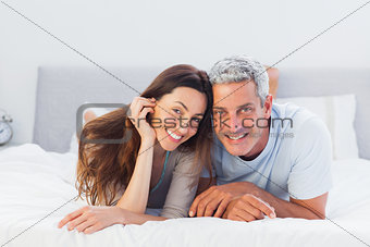 Couple lying on bed and smiling at camera