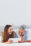 Smiling couple lying on bed using their tablet pc