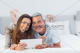 Cheerful couple lying on bed using their tablet pc
