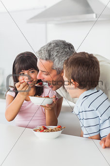 Siblings sharing cereal with their father