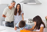 Cute siblings drawing together in kitchen with their parents smiling