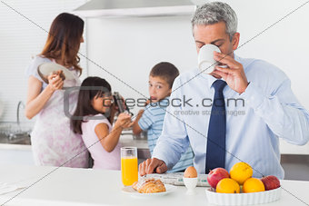 Father drinking coffee while his family are cooking in the kitchen