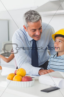 Father showing son his blueprints as he is wearing yellow helmet