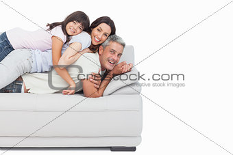 Smiling little girl lying on her parents on sofa