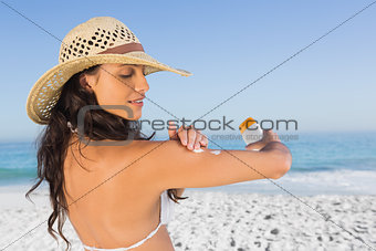 Attractive brunette with straw hat putting on sun cream