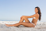 Cheerful attractive brunette in white bikini posing while sitting