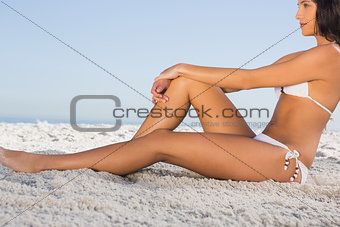Thoughtful attractive woman in white bikini posing while sitting