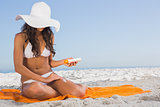 Attractive dark haired woman applying sun cream while sitting on her towel