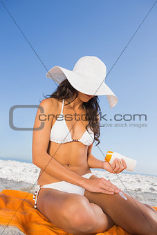 Sexy woman applying sun cream while sitting on her towel