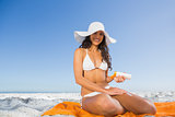 Cheerful sexy woman applying sun cream while sitting on her towel