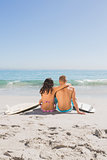 Beautiful young couple sitting with their surfboards
