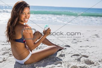 Smiling woman in bikini applying sun cream on her shoulder