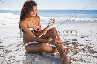 Smiling woman in bikini applying sun cream on her leg
