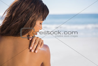 Pensive woman applying sun cream on her shoulder