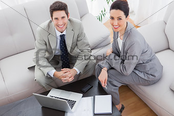 Smiling colleagues working together sitting on sofa and using laptop