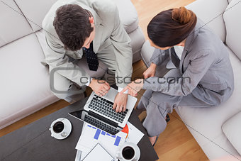 Coworkers using laptop together sitting on sofa