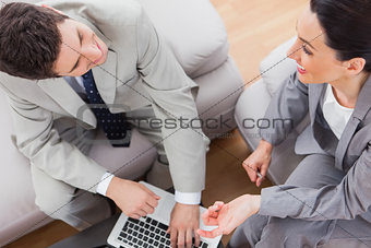 Smiling coworkers talking and using laptop sitting on sofa