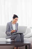 Happy busineswoman sitting on sofa using laptop
