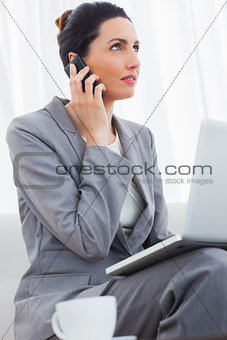 Businesswoman calling with her mobile phone and using laptop sitting on sofa