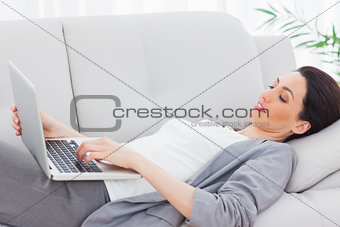 Smiling businesswoman lying on sofa using laptop