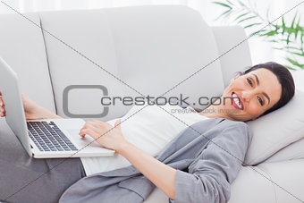 Happy businesswoman lying on sofa using laptop