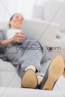 Businesswoman lying on sofa with her laptop