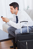 Businessman with his suitcase using mobile phone