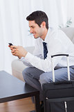 Businessman with his suitcase using mobile phone smiling