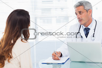 Serious doctor talking with his patient and writing on a notebook