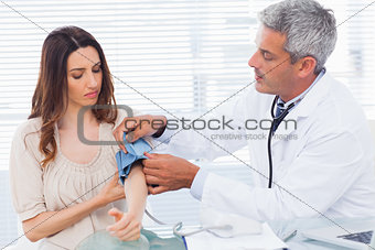 Serious doctor taking blood pressure of his patient