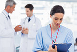 Nurse writing on a clipboard while doctors are talking together