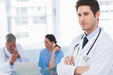 Serious doctor looking at camera with colleagues behind