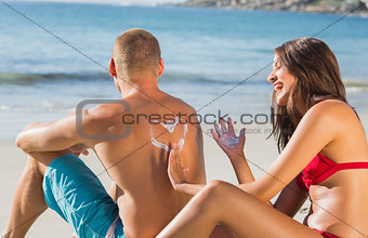 Cheerful attractive woman applying sun cream on her boyfriends back