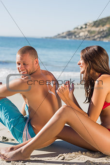 Woman drawing heart pattern with sun cream on her boyfriends back