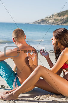 Smiling woman drawing heart pattern with sun cream on her boyfriends back